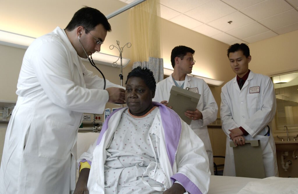 A physician examines a patient during a routine clinical checkup, with colleagues observing