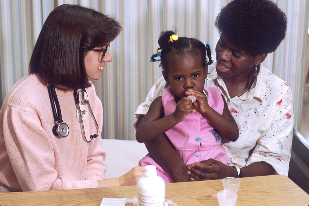 A nurse communicates health guidance to a mother holding her young daughter