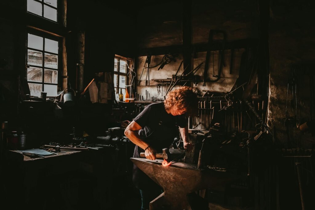 A craftsman forges metal at an anvil in a small workshop, representative of a family-run manufacturing business