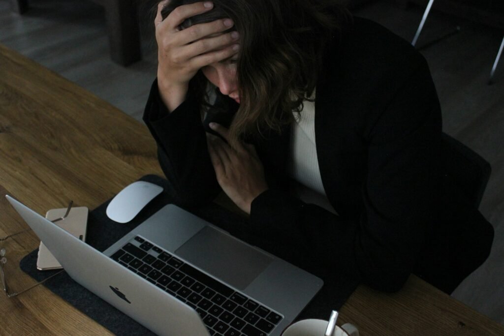 A worker sitting at a laptop with her head in her hands