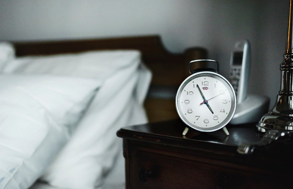 A bedside alarm clock in a dimly lit bedroom, representing healthy sleep and wake schedules.