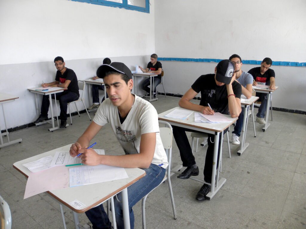 Rows of candidates seated at individual desks writing an examination in a large hall.