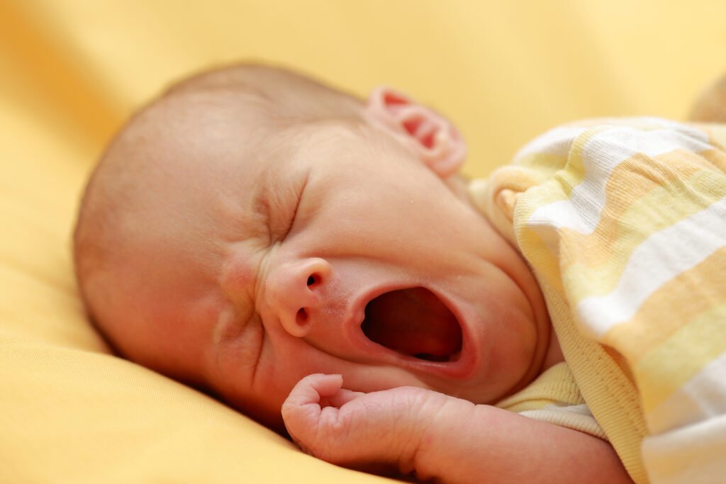 A person yawning widely, mouth open and eyes closed, illustrating the involuntary reflex of yawning.