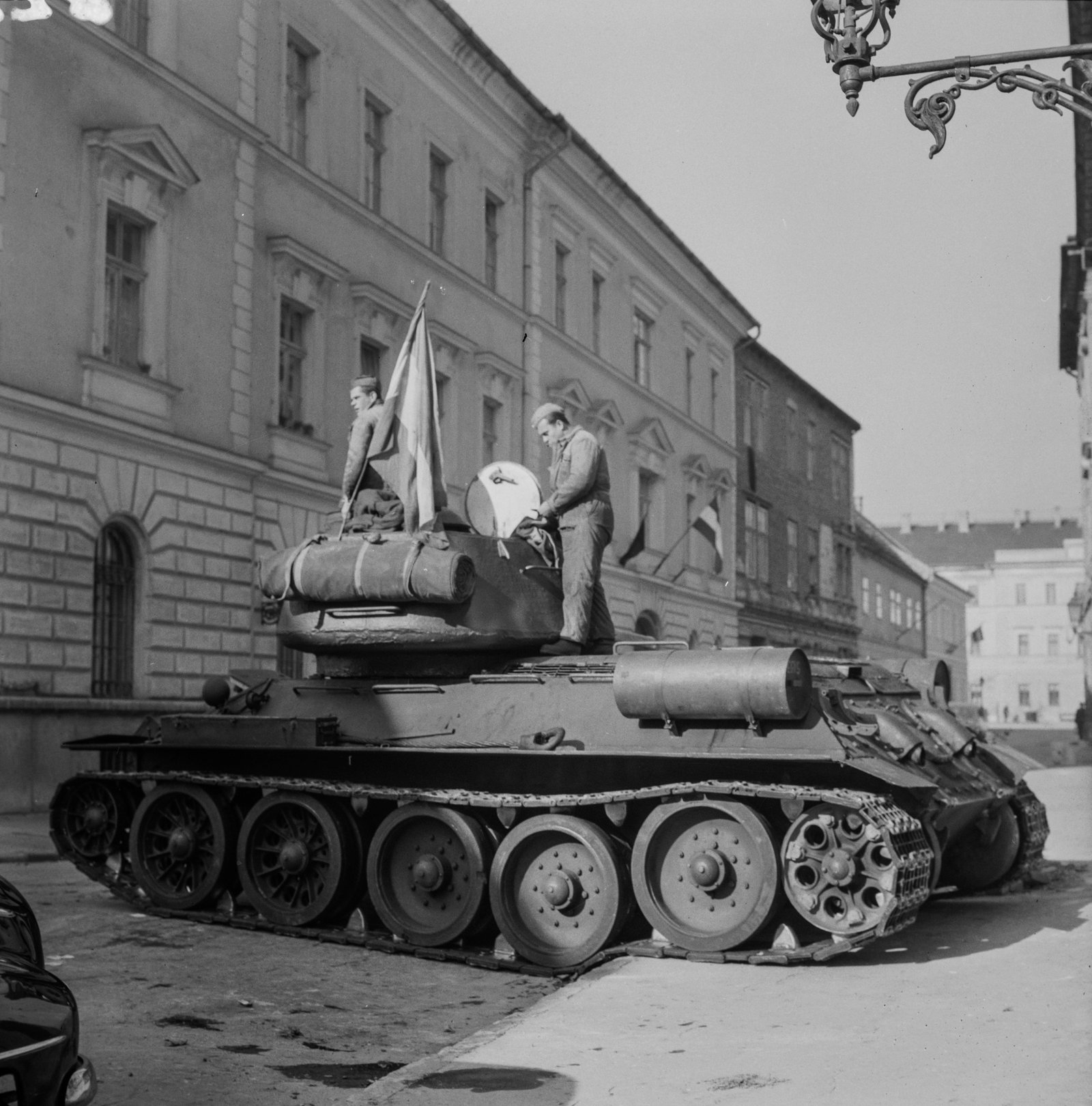 Black-and-white photograph of a Soviet T-34 tank parked in a Budapest street during the 1956 Hungarian uprising, with damaged buildings in the background.