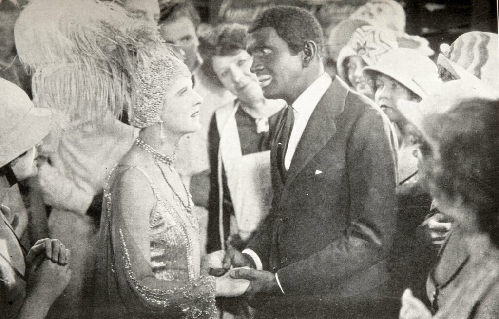 Black-and-white film still from The Jazz Singer (1927): Al Jolson, as Jack Robin, embraces May McAvoy, as Mary Dale, in a backstage scene.